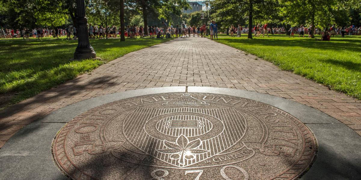 Picture of the seal of The Ohio State University on a sign with a brick building in the background.