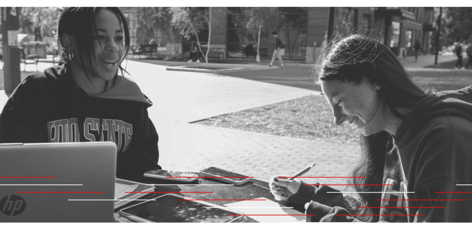Two students sitting outside laughing and working